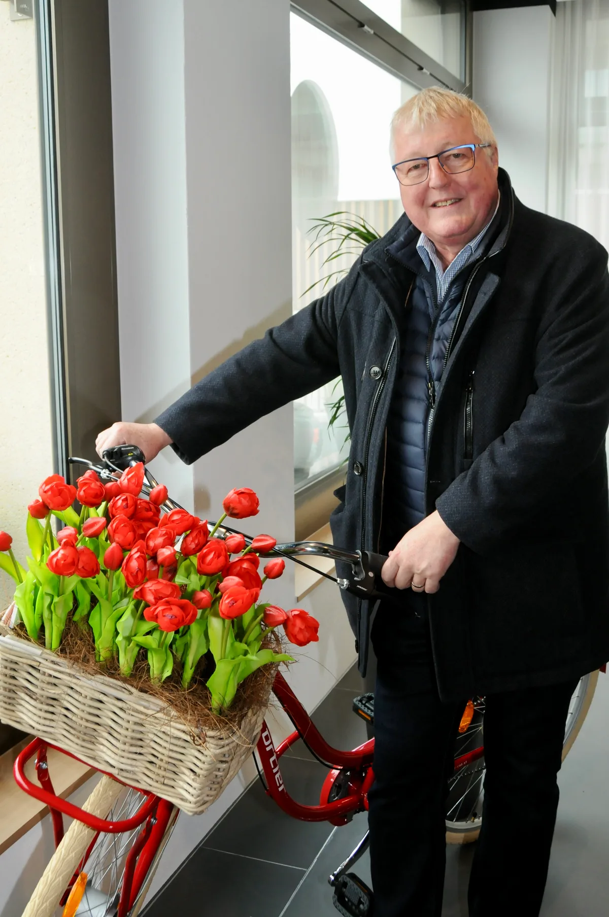 Man sieht Armin Pfiffner mit einem Velo, das mit roten Tulpen bepackt ist.